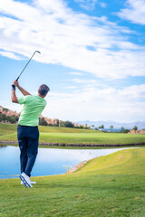 Man playing golf at golf club by a lake, hitting the ball