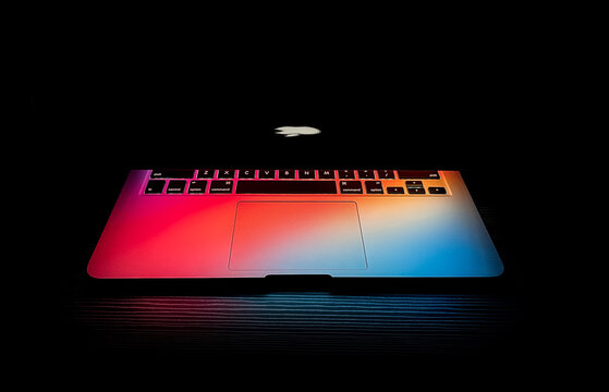 Apple macbook Laptop with backlit logo, half lid open on a table lit with colorful desktop screen wallpaper in a dark room, backlit keyboard, on July 12, 2021 in Dubai, United Arab Emirates	