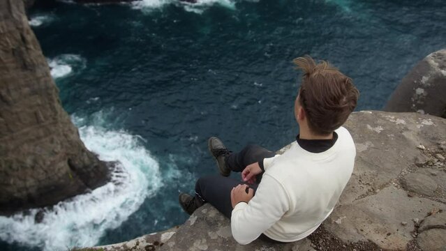 Scenic view of the Leitisvatn lake in Faroe Islands with a male sitting on the edge of a cliff