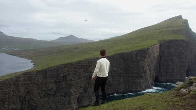 Scenic view of the Leitisvatn lake in Faroe Islands with a male standing on the edge of a cliff