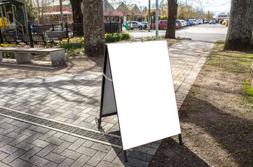 Blank white mockup template of an advertising sandwich easel board on a paved pedestrian walkway in an urban park with a car park and buildings in the background. Copy space for your design.