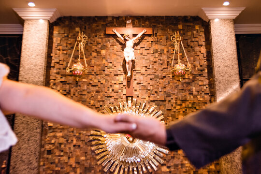 A wedding couple holding hands at the altar with images of Christ in the background