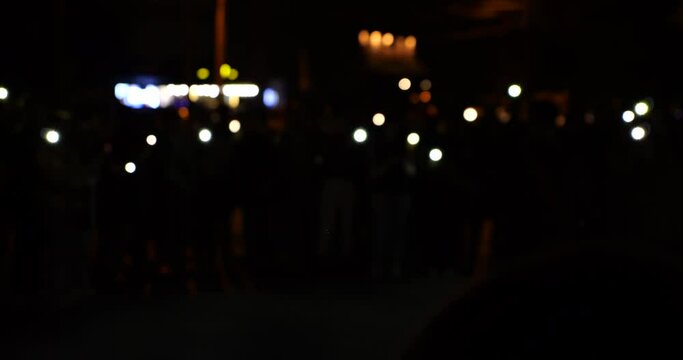 People with flashlights from smartphones dance to the music in the night city.
