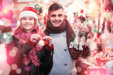 Positive young couple in Christmas hat with purchases at Christmas Fair outdoor