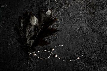 Black leaves and silver beads on a dark background. Black halloween concept