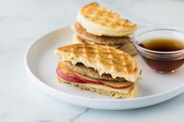 A waffle and sausage sandwich served with maple syrup for dipping.