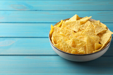 Tortilla chips (nachos) in bowl on light blue wooden table. Space for text