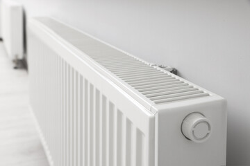 Modern radiator on white wall in room, closeup. Central heating system