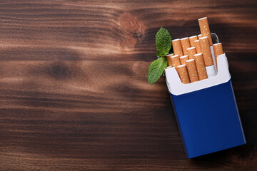 Pack of menthol cigarettes and mint leaves on wooden table, flat lay. Space for text