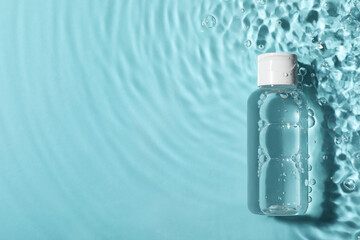 Fototapeta Wet bottle of micellar water on light blue background, top view. Space for text obraz