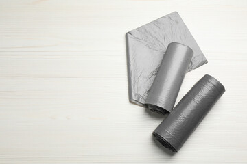 Fototapeta premium Rolls of grey garbage bags on white wooden table, flat lay. Space for text