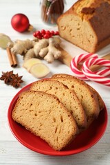 Slices of delicious gingerbread cake, ingredients and candy canes on white wooden table