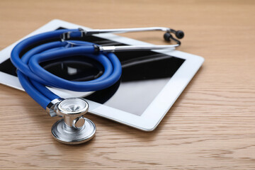 Computer tablet with stethoscope on wooden table, closeup