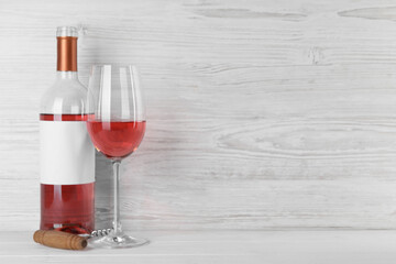 Corkscrew near bottle and glass of delicious rose wine on table against white wooden background. Space for text