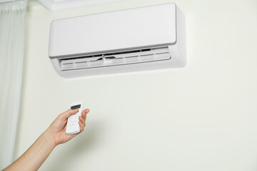 Fototapeta premium Man operating air conditioner with remote control indoors, closeup