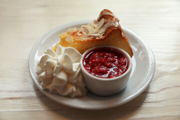 Piece of delicious cake with whipped cream and jam on white wooden table, closeup