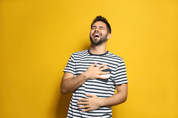 Young man laughing on yellow background. Funny joke - obrazy, fototapety, plakaty