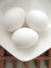 tres huevos blancos en un bol blanco, sobre rejilla de madera