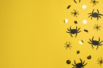 Flat lay composition with spiders and golden confetti on pale yellow background, space for text. Halloween celebration