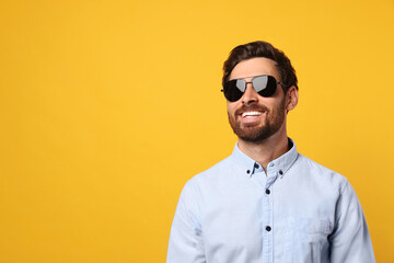 Portrait of smiling bearded man with stylish sunglasses on orange background. Space for text