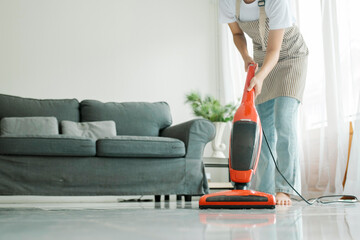Young woman cleaning house with vacuum cleaner. - obrazy, fototapety, plakaty
