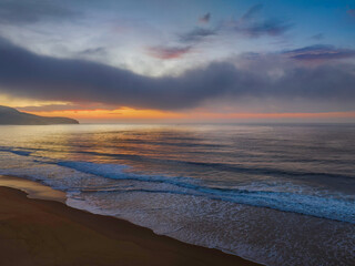 Fototapeta Peaceful sunrise over the ocean with small waves, clouds and fog rolling across obraz
