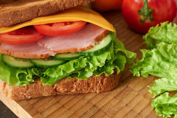 Ham sandwich close-up view from the side on a nice wooden background with tomatoes and lettuce leaves. 
