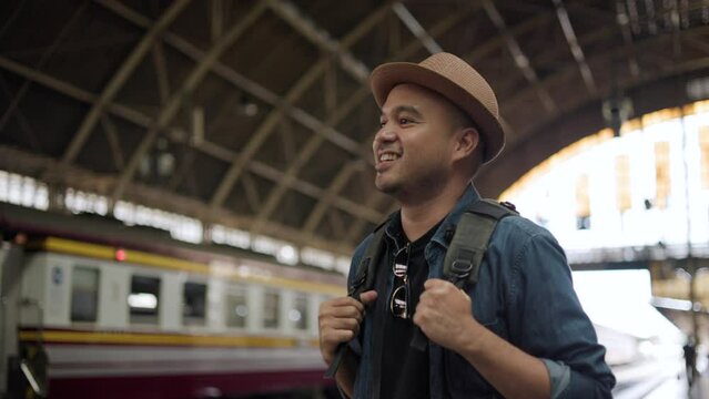 Freedom traveler young asian man at terminal train station. Happy tourist travel by train on vacation time holiday weekend trip. Male Backpacker arrival at platform railway. Go Everywhere concept.