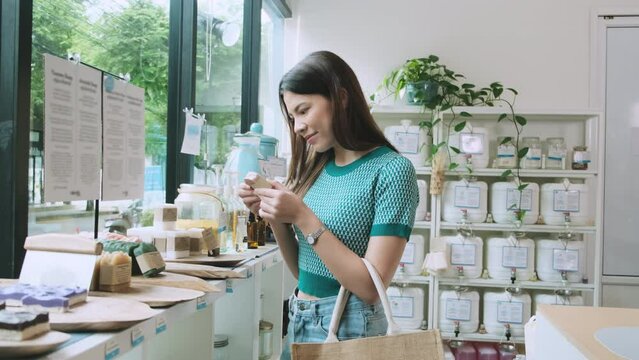 Young Caucasian female customer is choosing and shopping for organic products in refill store with reusable bag, zero-waste grocery, and plastic-free, eco environment-friendly, sustainable lifestyles.