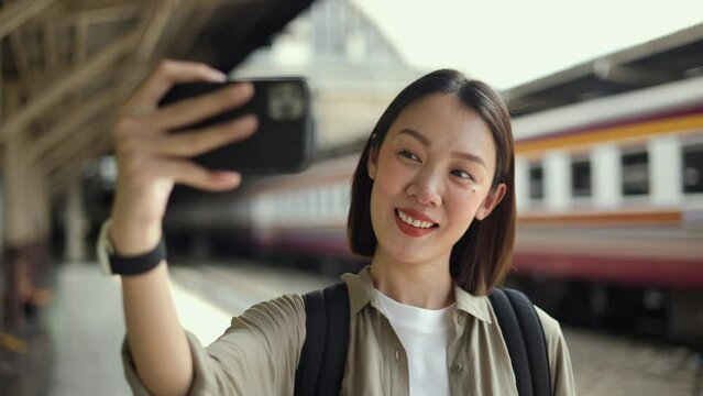 Freedom traveler young asian woman hanging handrail on train and taking photo by smartphone. Happy tourist travel by train on vacation time holiday weekend trip. Backpacker arrival at platform railway