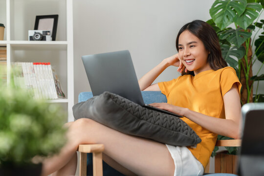 Cheerful young woman wear orange shirt with sitting on sofa and using laptop computer at home.