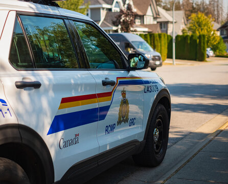 RCMP vehicle stopped on a street. The door logo crest of a white Royal Canadian Mounted Police RCMP cruiser