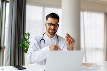 Portrait of young doctor talking to online patient on laptop screen sitting at clinic office desk giving online consultation for domestic health treatment. Telemedicine remote medical appointment