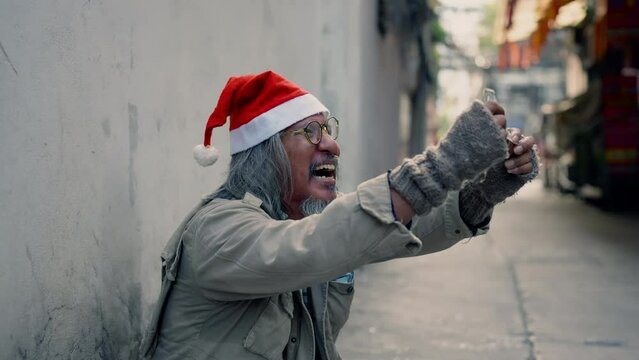 Asian homeless psychopath mad man wearing christmas hat sitting on wayside with hope, dirty alcoholism aged man retirement with beard crying on street begging for money, no job.
