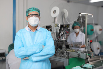 Worker in personal protective equipment or PPE inspection quality crossed arms and looking camera in mask and medical face mask production line factory, manufacturing industry and factory concept.