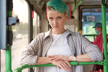 woman with green hair and white clothes rides a bus.