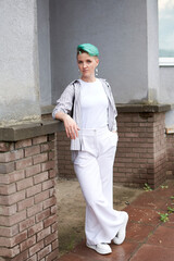 A woman with green hair in white clothes and with an umbrella walks down the street after the rain