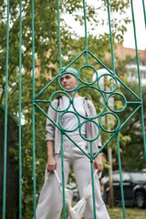 A woman with green hair in white clothes and with an umbrella walks down the street after the rain