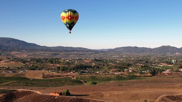 Colorful Hot Air Balloon Flying Above Sunny Valley and Small Town in Countryside of California USA, Aerial View