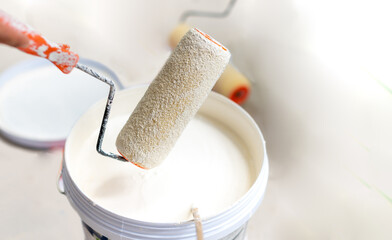 The female hand use the woodstick to mix paint into the tray and dips roller.