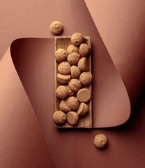 Tasty chocolate truffles in a wooden dish on a brown background.
