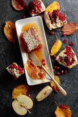  Honeycomb, apples, and pomegranate on a black stone table.