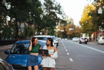 Two young women with a laptop near the car