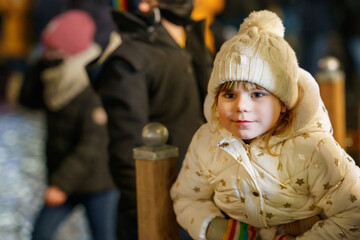 Fototapeta na wymiar Cute little preschool girl on winter evening on christmas market. Happy smiling child in warm clothes. Joyful kid portrait