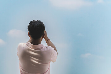 Back view of man using cell phone to take photo with cloud and sky in background. Asian male rests...