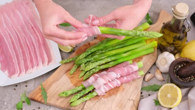 Woman Cooking asparagus wrapped with bacon at domestic kitchen