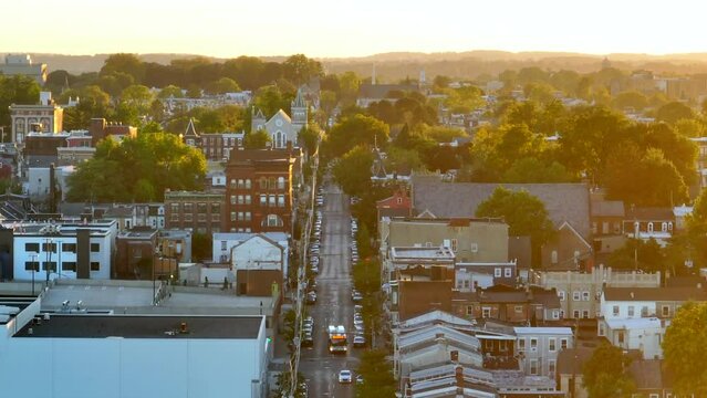 Warm glow of autumn light. American suburb and downtown city region. Houses and homes among fall foliage on trees. Rising aerial long zoom lens.