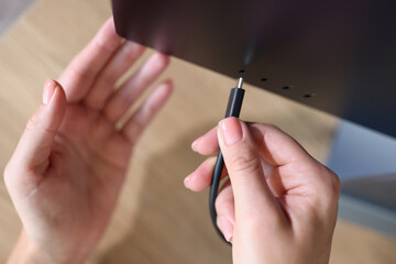 Person hand connects a black USB-C or Type C power cable to computer