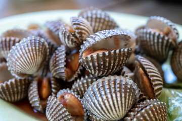 Steamed cockle or Boiled cockles on the dish with spicy seafood sauce and vegetable in restaurante wooden background