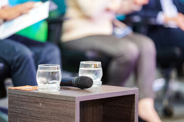 two glasses of water are prepare to speakers who sit on the stage with microphone beside it.